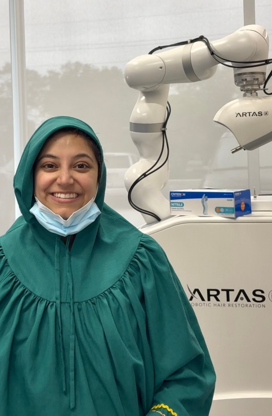Dr. B in surgical gown beside the ARTAS iX robotic hair restoration system at HairBotMD in Cypress, Texas